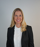 20160502 Hallwig Sabine 2 Eine lächelnde Frau mit langen, blonden Haaren trägt einen schwarzen Blazer und eine weiße Bluse mit Rüsche. Der Hintergrund ist neutral und helle Farben, was den Fokus auf die Person legt.