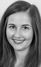 Eine junge Frau mit langen, braunen Haaren lächelt in die Kamera. Sie trägt ein leicht glitzerndes Oberteil und hat einen warmen, freundlichen Ausdruck. Der Hintergrund ist einfarbig und neutral.