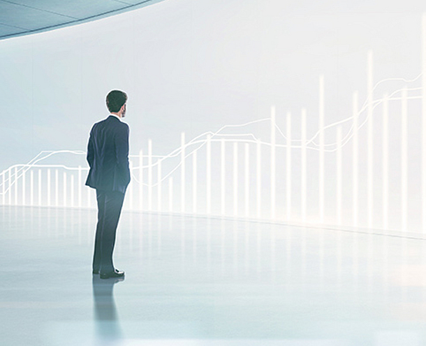 Ein Mann in Anzug steht vor einer hellen Wand, auf der grafische Linien und Balken dargestellt sind, die einen Anstieg zeigen. Er blickt nachdenklich auf diese visuelle Darstellung, die Fortschritt und Wachstum symbolisiert.